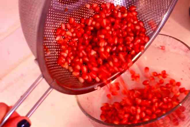 Pomegranate seeds pouring out of strainer